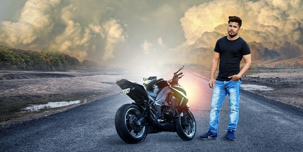 Cheerful biker poses to have break after driving, poses near black motorbike,  holds protective helmet, yellow trees and leaves around, enjoys good  weather. Autumn season. Urban lifestyle. Outdoor shot 7909340 Stock Photo